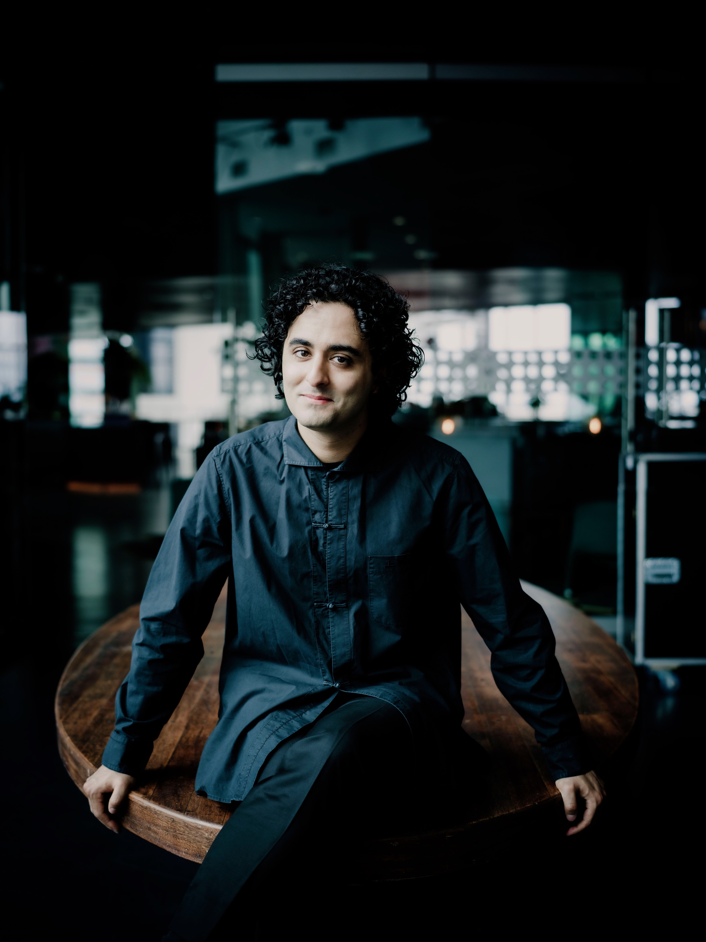 Kerem Hasan seated on a wooden table in a dark blue shirt