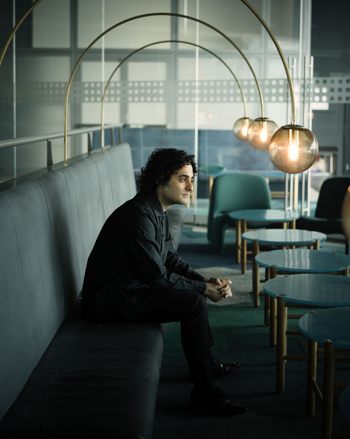 Kerem Hasan seated beneath curved brass lamps
